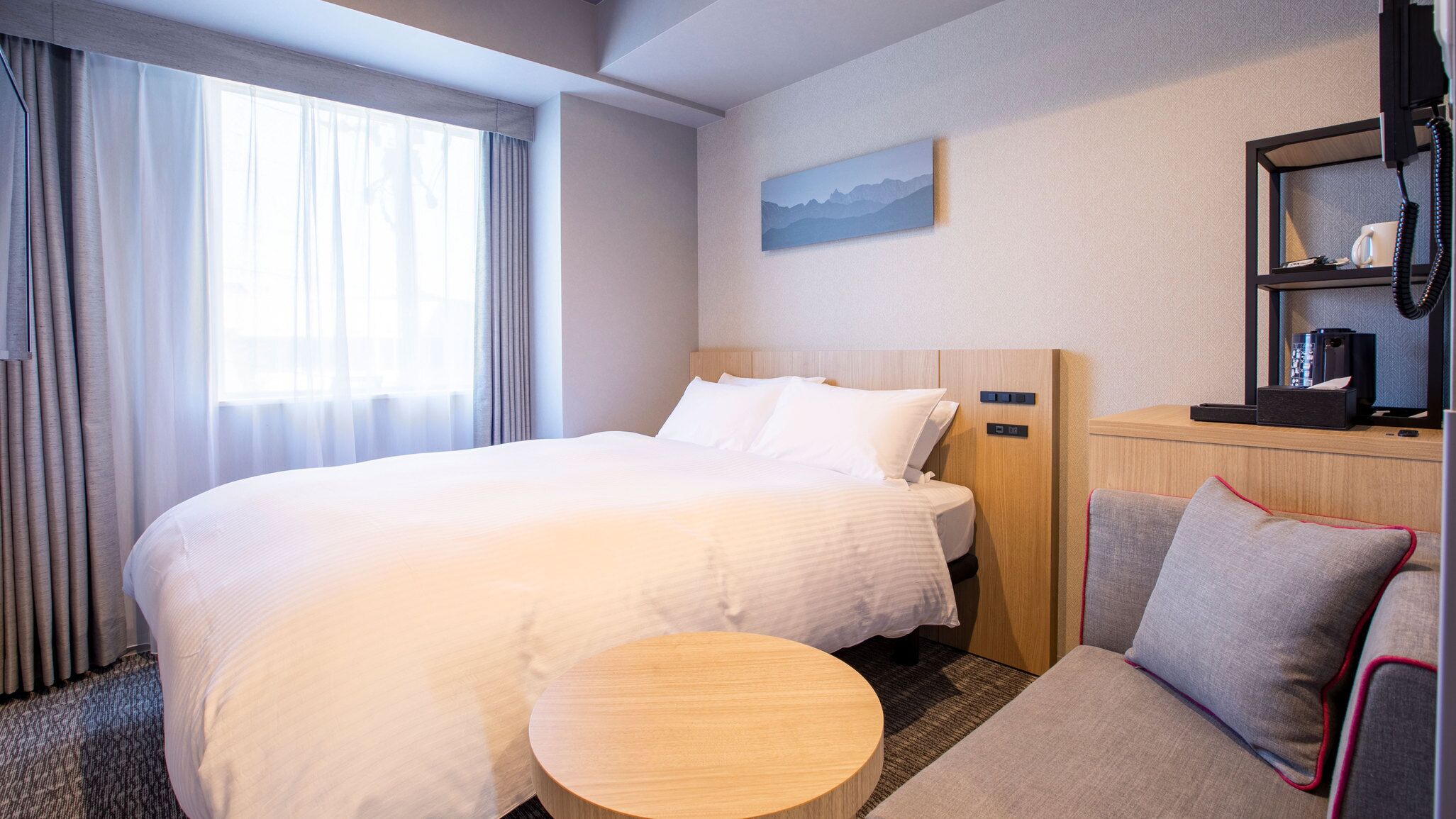 Ein Hotelzimmer mit einem großen Bett, einem kleinen runden Tisch, einer Couch, einem Bild an der Wand und einem Regal mit Telefon und Kaffeemaschine.