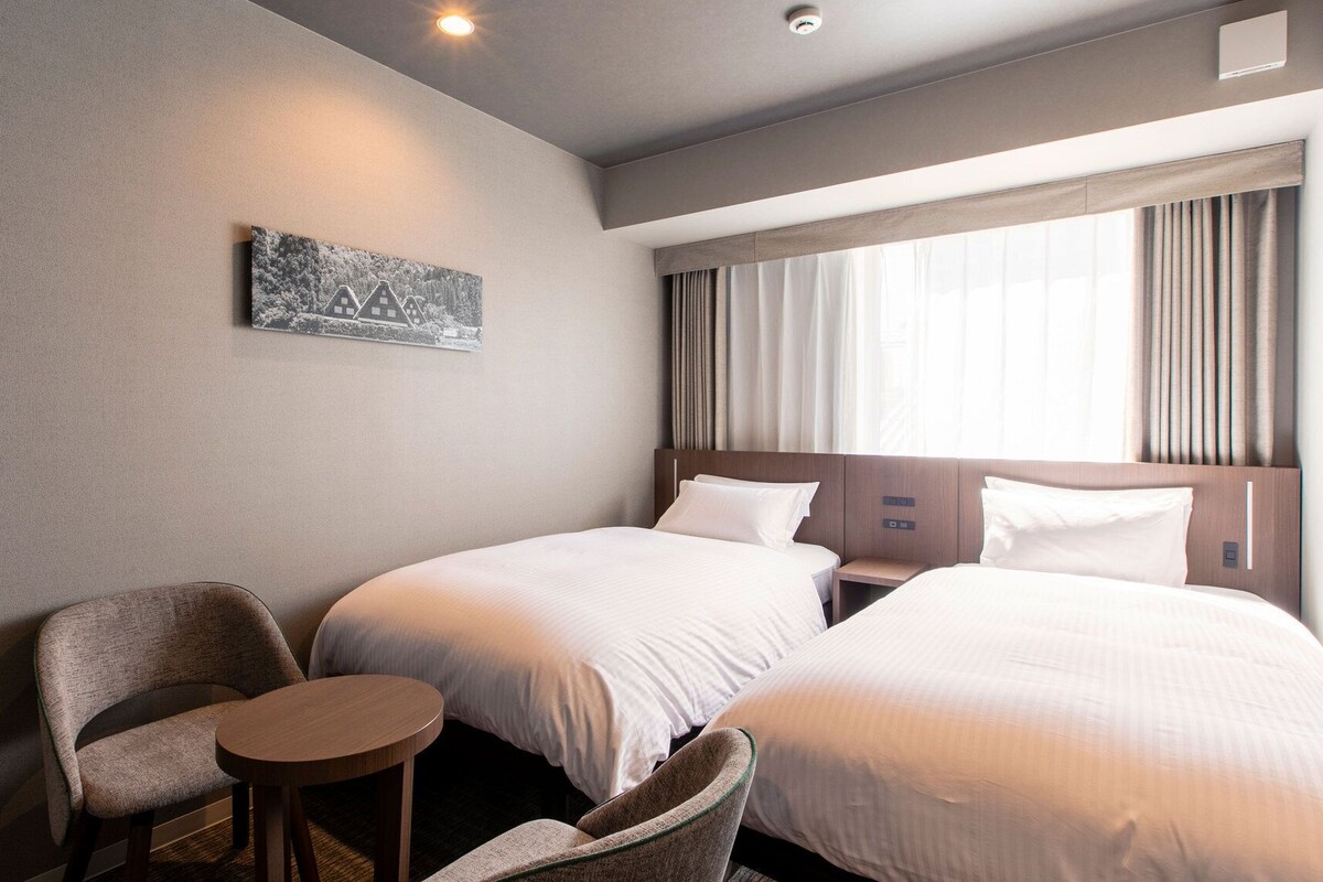Ein Hotelzimmer mit zwei Betten, einem kleinen Tisch, einem Stuhl und einem Bild an der Wand.