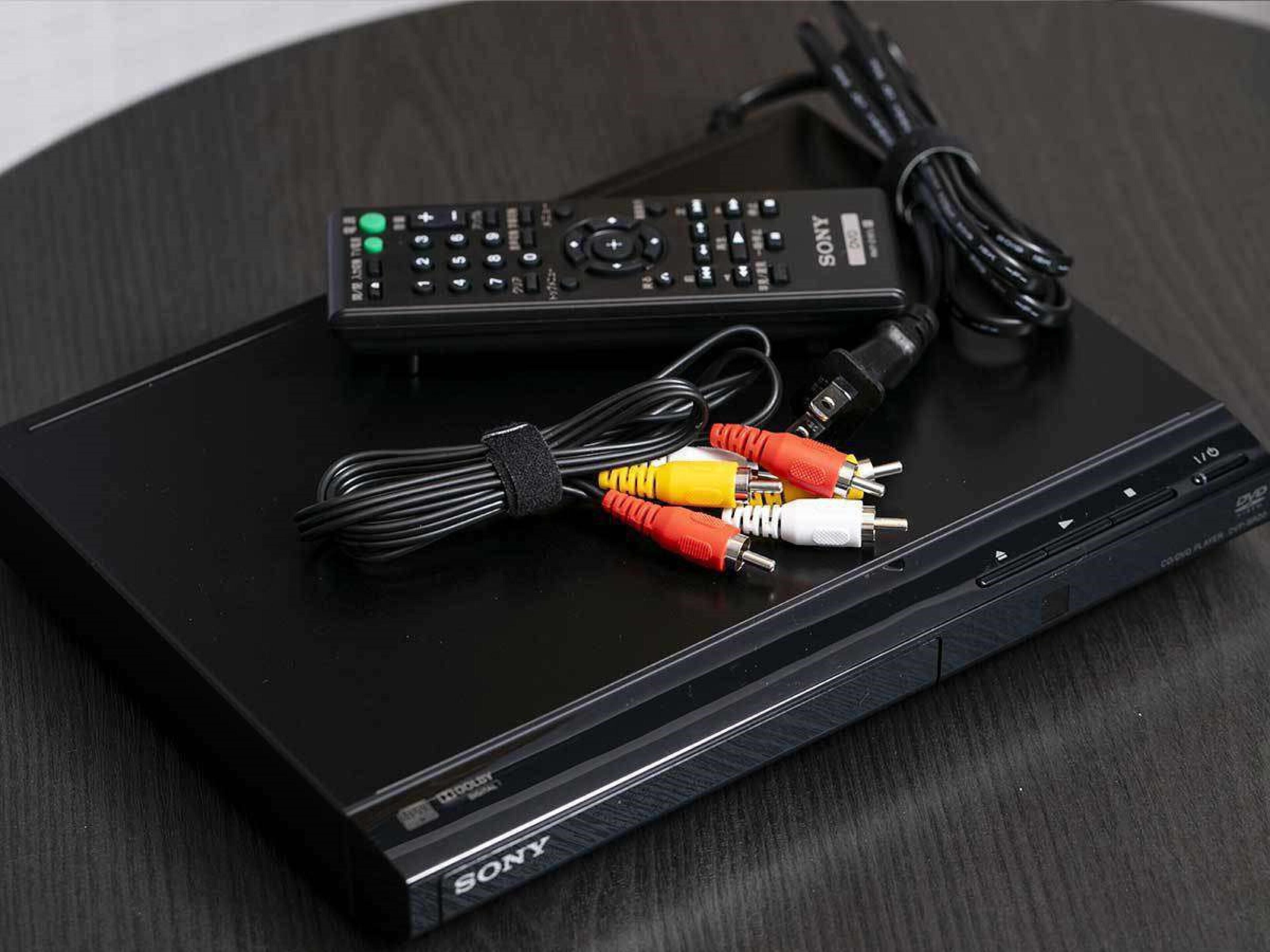 A black Sony portable media player with a remote control and a set of audio cables on a dark wooden surface.