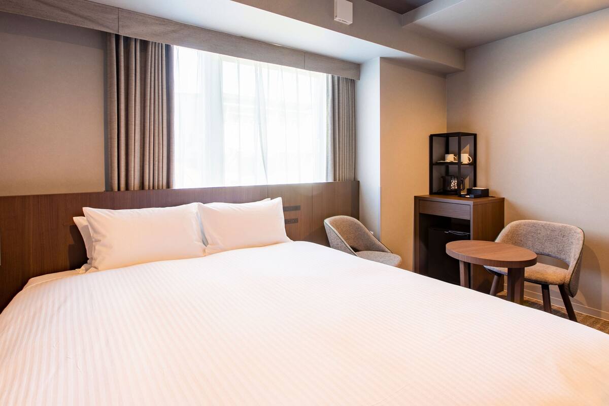 Een hotelkamer met een groot bed, een bureau met stoel, een klein tafeltje en een plank met spullen.