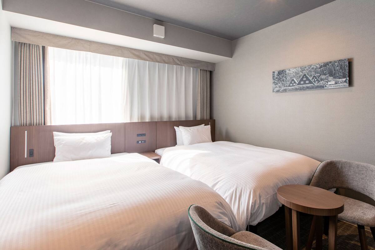 Een hotelkamer met twee bedden, een klein tafeltje, een stoel en een schilderij aan de muur.