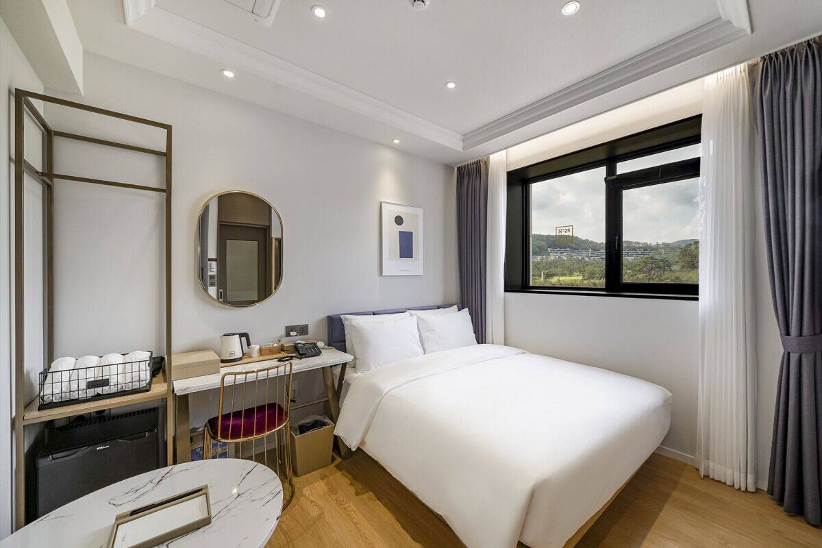 A hotel room with a bed, desk, chair, and a window with a view.