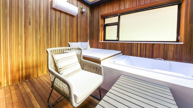 A modern bathroom with a bathtub, a wicker chair, and a wooden floor. - Gijang No.25 Hotel (Busan)