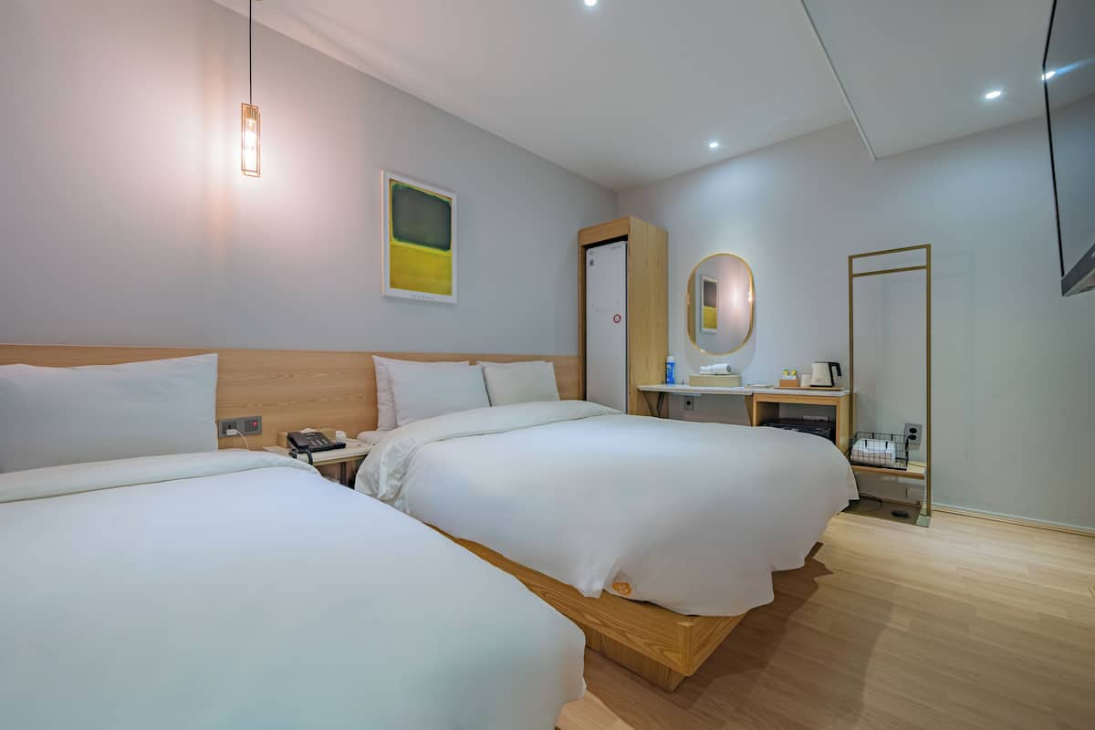 A hotel room with two beds, a bedside table with a phone, a mirror, and a small desk with a lamp and a coffee maker.