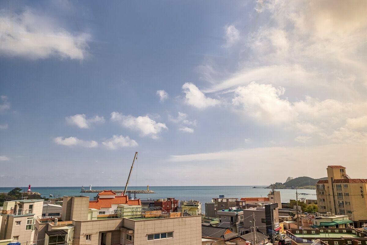 A coastal cityscape with buildings, a crane, and a lighthouse in the distance.