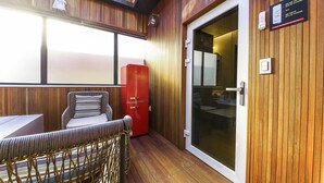 A wooden-paneled room with a wicker chair, a red cabinet, and a sliding glass door. - Gijang No.25 Hotel (Busan)