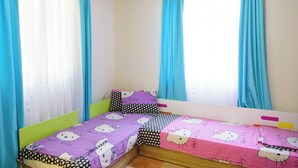 Una habitación pequeña con cama individual, techo inclinado y dos ventanas con cortinas azules.