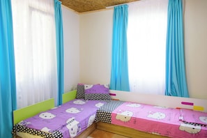 Une petite chambre avec un lit simple, un plafond en pente et deux fenêtres ornées de rideaux bleus.