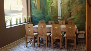 Un comedor con sillas de madera y una mesa, un mural en la pared y una ventana con plantas.