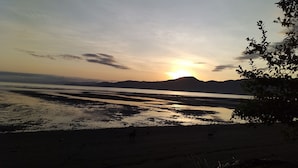 En strand ved solnedgang, roligt vand og fjerne bjerge.