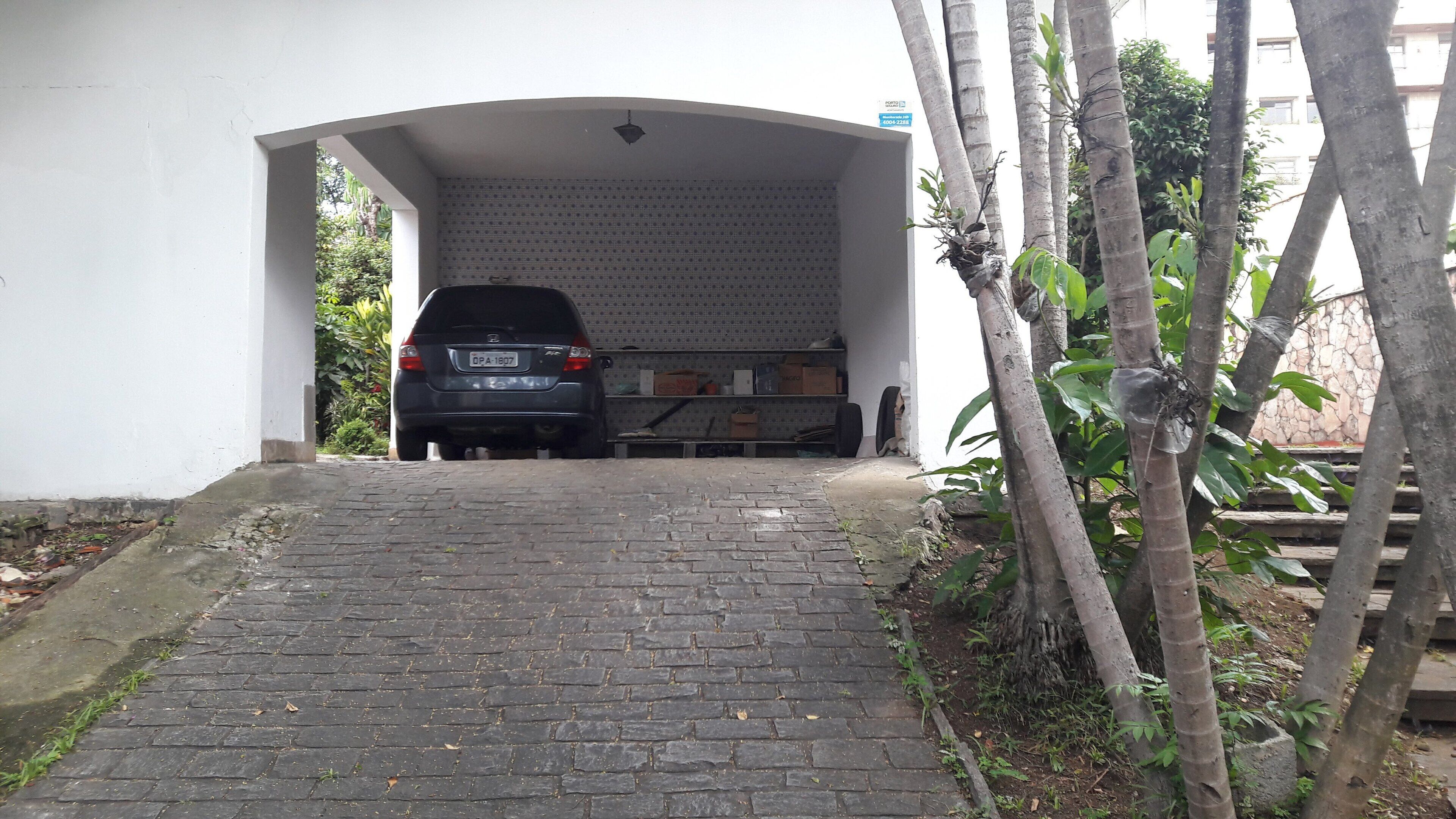 Une voiture est garée à l’intérieur d’un garage fermé, et un chemin pavé de briques mène à l’entrée.