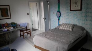 Un dormitorio con una cama, un escritorio y una silla. Hay una puerta que da a otra habitación.