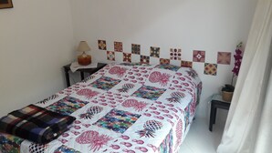 Un lit bien fait, recouvert d’une courtepointe à motifs floraux, une table de chevet avec une lampe, et un mur décoré de carreaux à motifs.