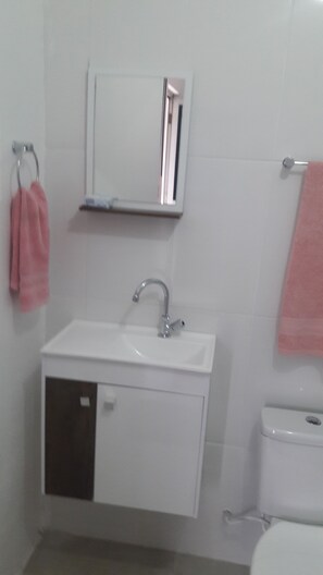 A bathroom with a white sink, a mirror above it, and a toilet. There are pink towels hanging on a rack. - Confortable Suite in a Cozy House Excelent Location and Transport Acess (São Paulo)