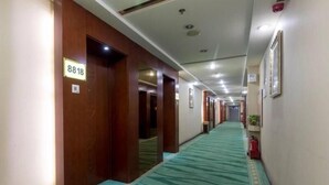 Un couloir d’hôtel avec un sol recouvert de moquette, des portes en bois et un extincteur sur le côté droit.