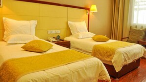 Une chambre d’hôtel avec deux lits, chacun étant équipé de draps blancs et d’un plaid jaune. On y trouve une table de chevet avec une lampe et un téléphone.