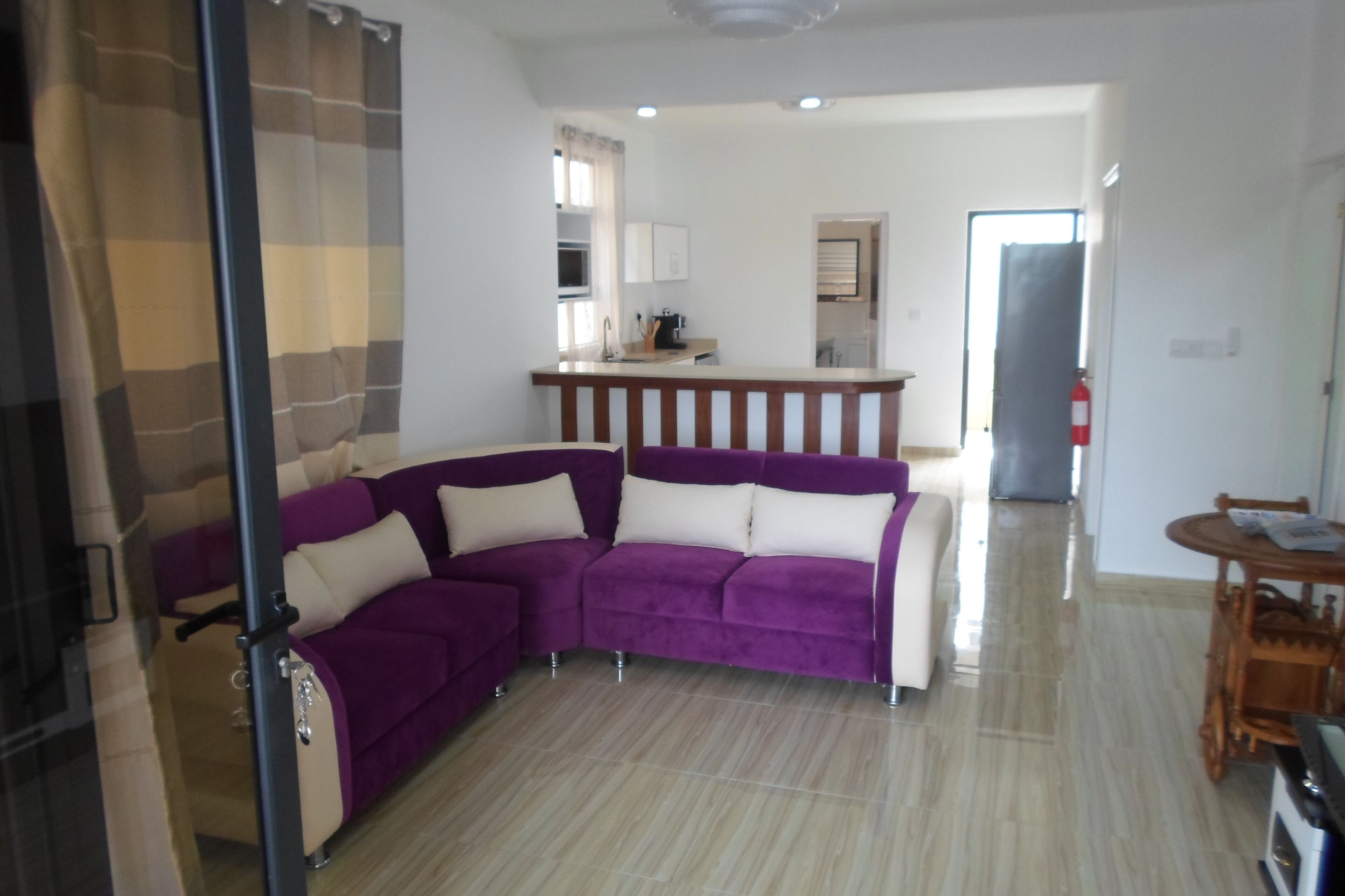 Een woonkamer met een paarse modulaire bank, een keuken op de achtergrond, en een eettafel met stoelen.