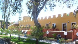 A courtyard with a yellow building, a large tree, and a small fountain. - Costa del Sole Apartment 50 Meters From the Beach of the Catania Coast (Catania)