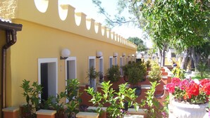 A courtyard with yellow walls, multiple doorways, and potted plants with flowers. - Costa del Sole Apartment 50 Meters From the Beach of the Catania Coast (Catania)