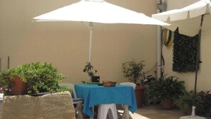 A patio area with a table covered by a blue tablecloth, surrounded by potted plants, and two white umbrellas providing shade. - Room-merzuq House - Deluxe Double Room w (Birzebbuga)