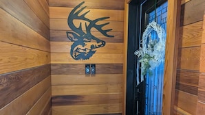 Un couloir étroit aux murs en bois, une tête de cerf décorative accrochée au mur et une porte ornée d’une guirlande.