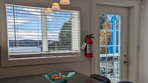 Un coin repas avec une table en verre, un saladier rempli de fruits et un extincteur fixé au mur.