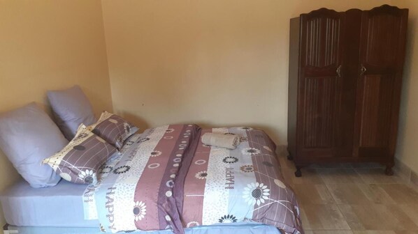 A bedroom with a bed, two pillows, a wooden wardrobe, and a tiled floor. - Karl Heyne Guesthouse Double Room (Rustenburg)