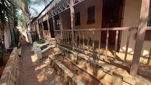 A covered outdoor area with a stone pathway leading to a building with a white railing and a wooden door. - Spacious Double Room in Lovely Guesthouse (Rustenburg)