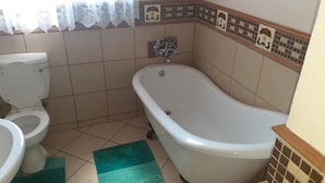 A bathroom with a toilet, a bathtub, and a green rug. - Spacious Double Room in Lovely Guesthouse (Rustenburg)