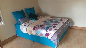 A bed with a floral-patterned bedspread, blue bedding, and multiple pillows. - Spacious Double Room in Lovely Guesthouse (Rustenburg)