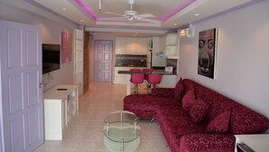 A modern living room with a red sofa, a glass coffee table, and a kitchen in the background. - Jomtien Beach Condominium 3rd Floor apt (Pattaya)