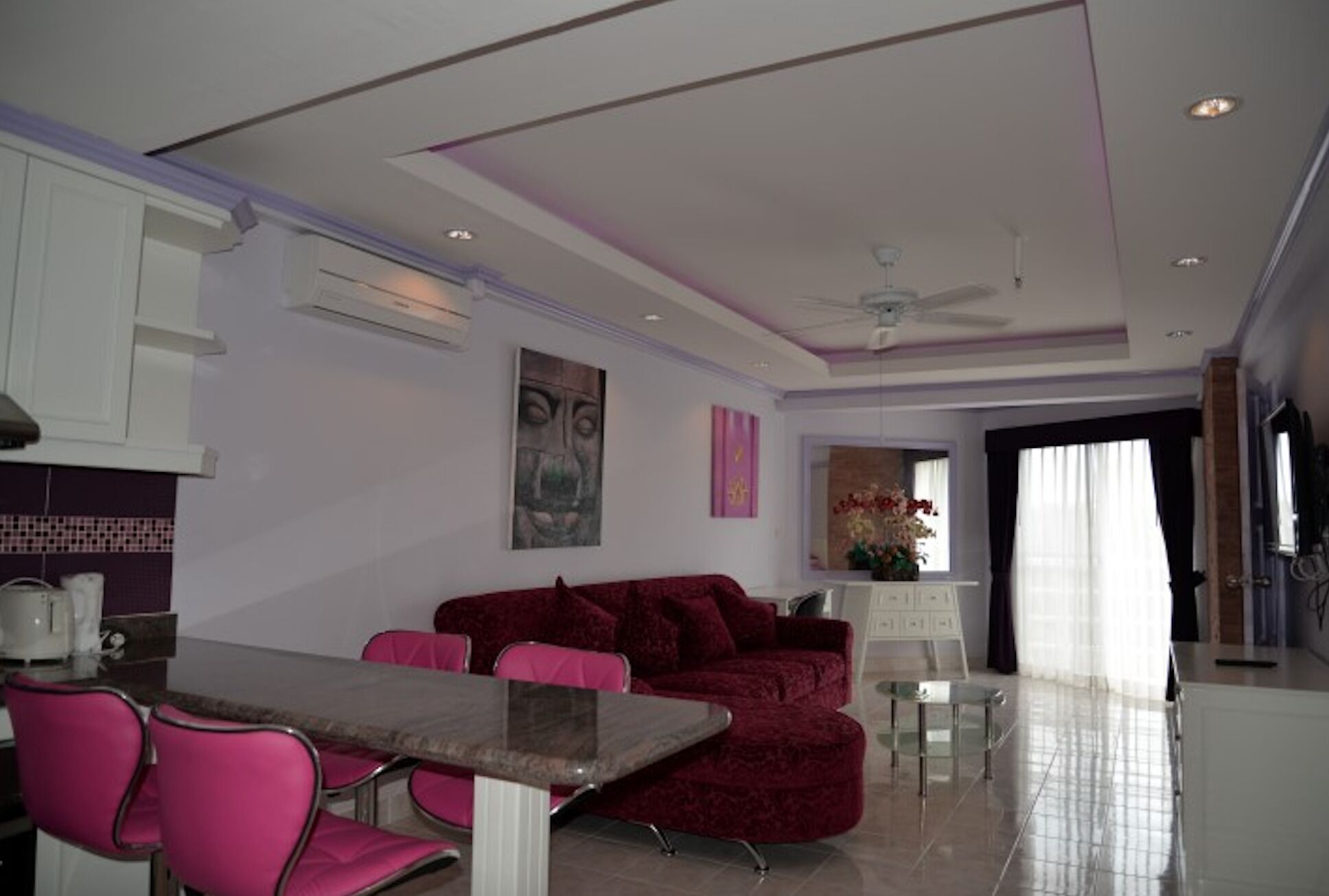 A modern living room with a red sofa, pink chairs, a dining table, and a ceiling fan.
