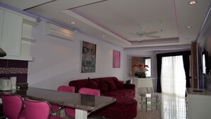 A modern living room with a red sofa, pink chairs, a dining table, and a ceiling fan. - Jomtien Beach Condominium 3rd Floor apt (Pattaya)