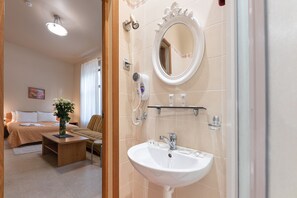 A hotel room with a bed, a sitting area, a bathroom with a sink and mirror, and a ceiling light.