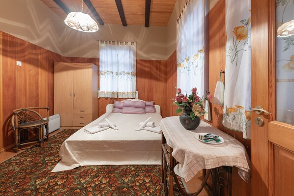 A bedroom with a bed, a chair, a table with a vase, and curtains.