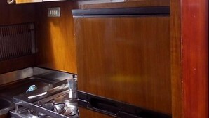 A compact kitchen with wooden cabinets, a stainless steel stove, and a refrigerator. - Akhir Cruise Charter (Salerno)