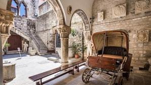 An interior courtyard with stone arches, a wooden carriage, and a bench. - Kind Room -hotel Rose Split (Split)