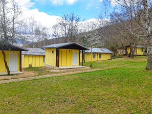 Une rangée de cabanes jaunes aux portes blanches, installées dans une zone herbeuse, avec des arbres et une montagne en arrière-plan.
