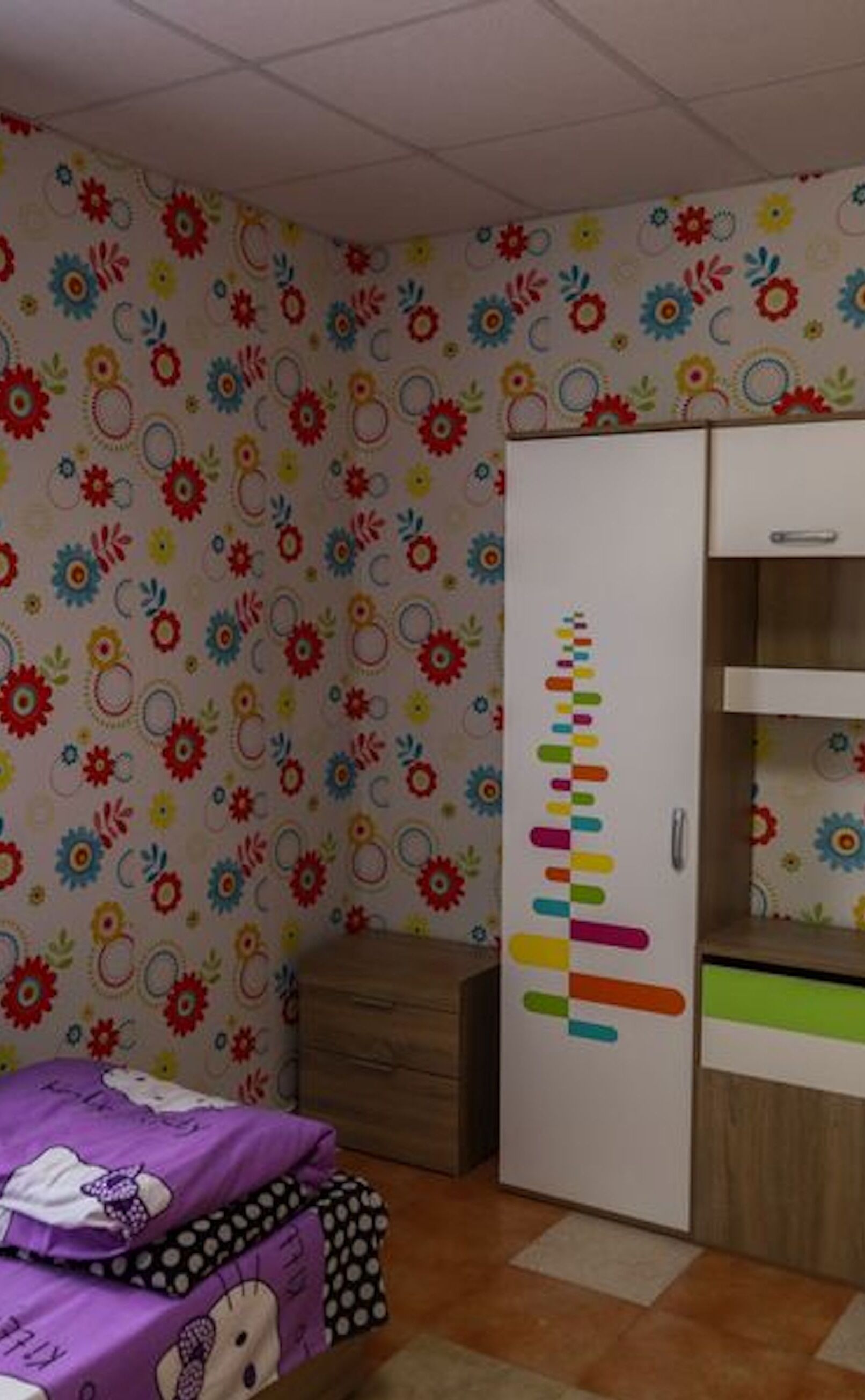 A bedroom with a bed, a wardrobe, and a wall with a floral pattern.