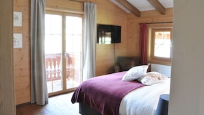 Ein Schlafzimmer einer Holzhütte mit Bett, Vorhängen, einem Fernseher und einem Balkon.