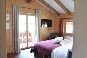 Un dormitorio de cabaña de madera con cama, cortinas, un televisor y un balcón.