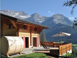 Una cabaña de madera con un barril grande, un patio con sillas y vistas a la montaña.