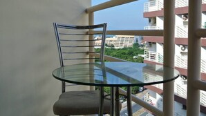 Mesa y silla de vidrio en un balcón con vista a un paisaje urbano.