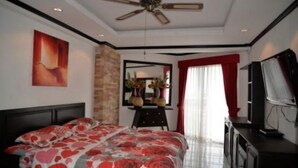 Un dormitorio con cama, ventilador de techo, televisor y ventana con cortinas.