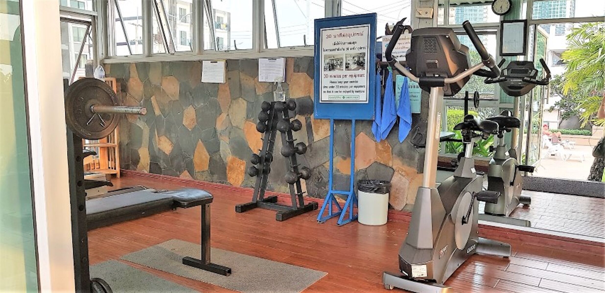 A gym with exercise equipment, a stone wall, and a bench.