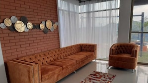 Uma sala de estar moderna com parede de tijolos, uma janela grande, um sofá, uma poltrona e arte decorativa na parede.
