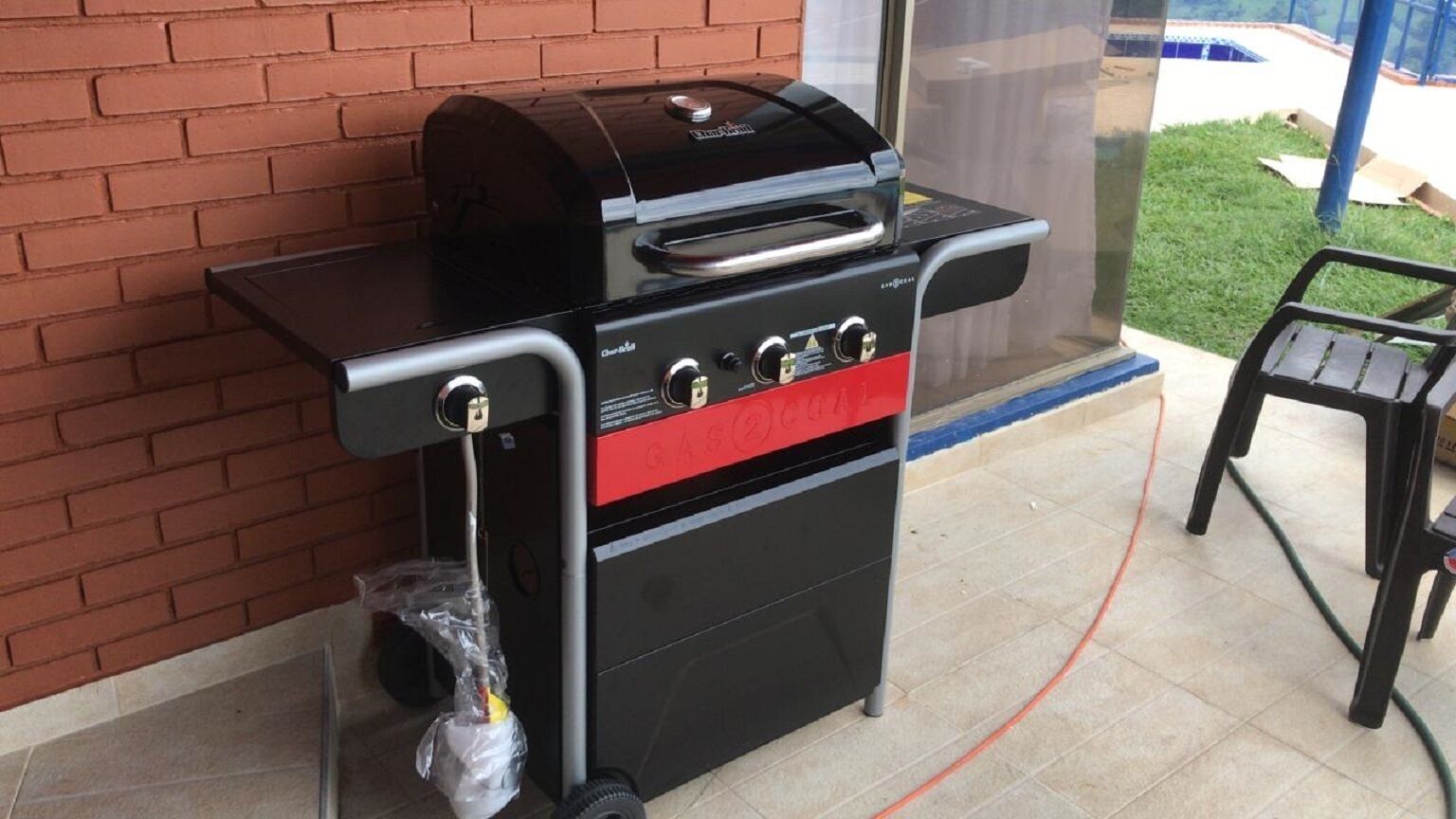 A portable gas grill with a digital display and control knobs, positioned against a brick wall.