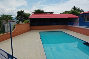 A rectangular swimming pool with a tiled deck and a red-roofed structure in the background. - Country House in Cerritos, Pereira (Pereira)