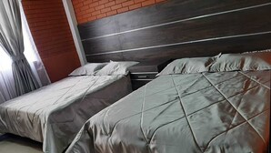 Quarto de hotel com duas camas, parede de tijolos e cabeceira moderna.