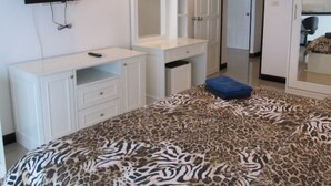 A bedroom with a bed, a vanity with a mirror, a television mounted on the wall, and a wardrobe.